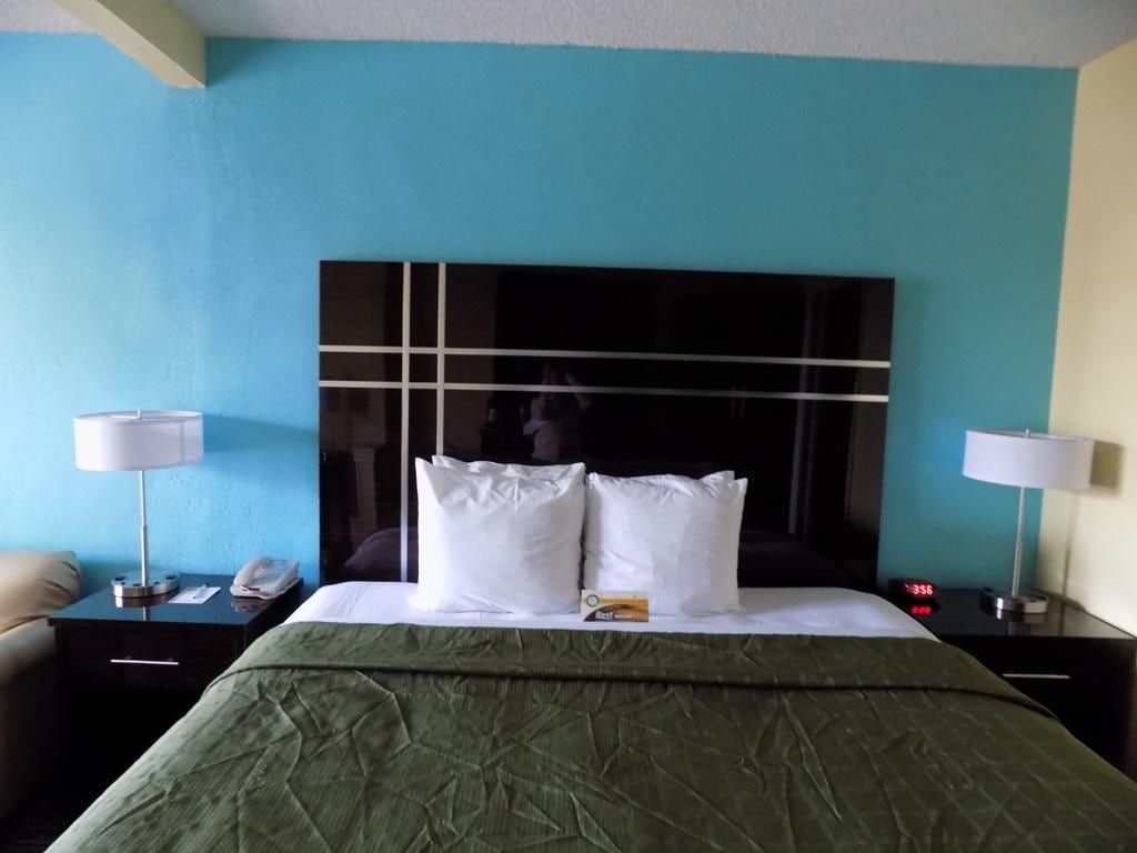 A hotel room with a bed, two bedside tables, a nightstand, a green bedspread, and a blue wall.