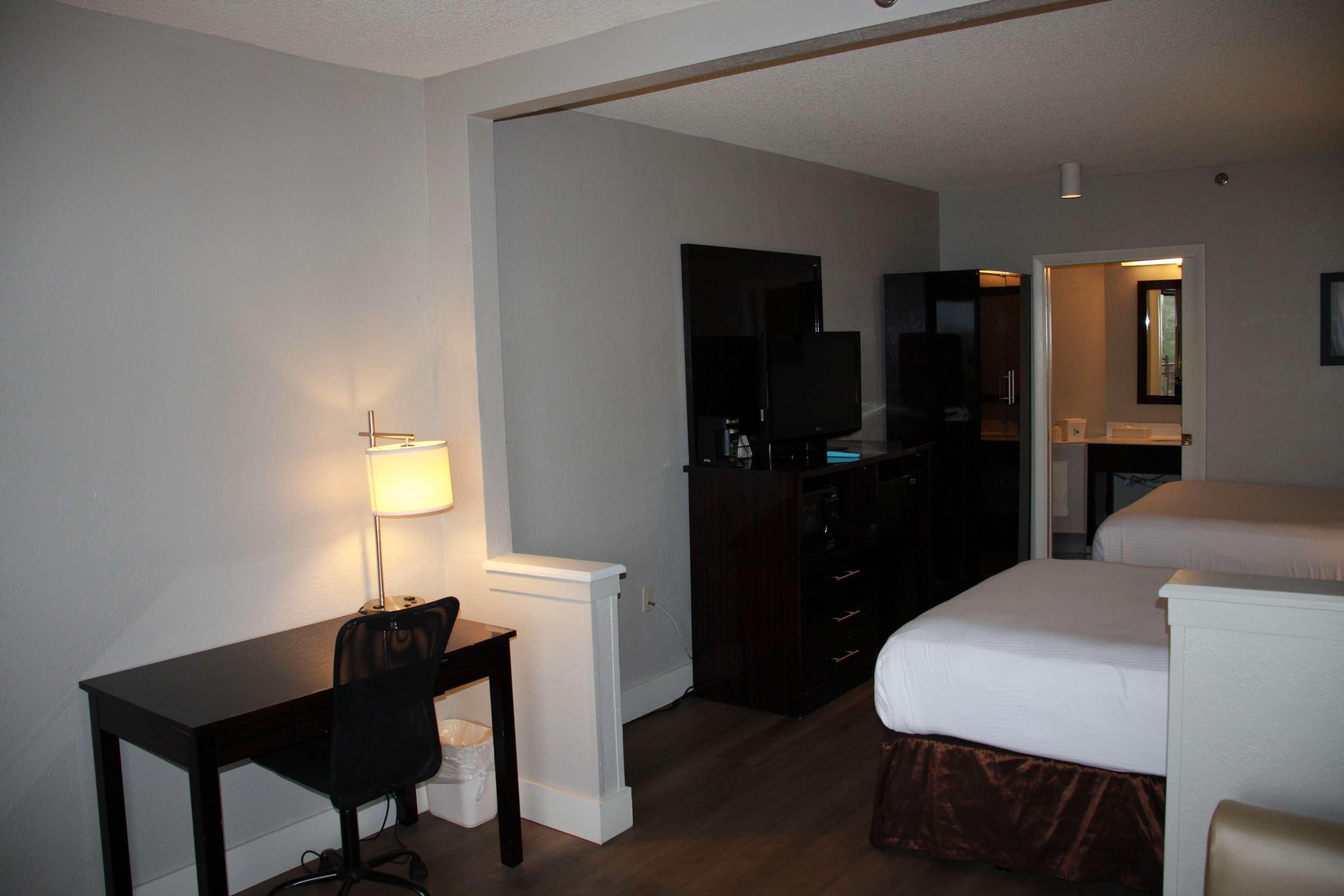 Habitación de hotel con escritorio, silla, televisor, cama y baño visible a través de una puerta abierta.