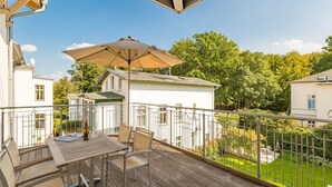 A balcony with a table and chairs, a large umbrella, and a view of a garden and neighboring buildings.