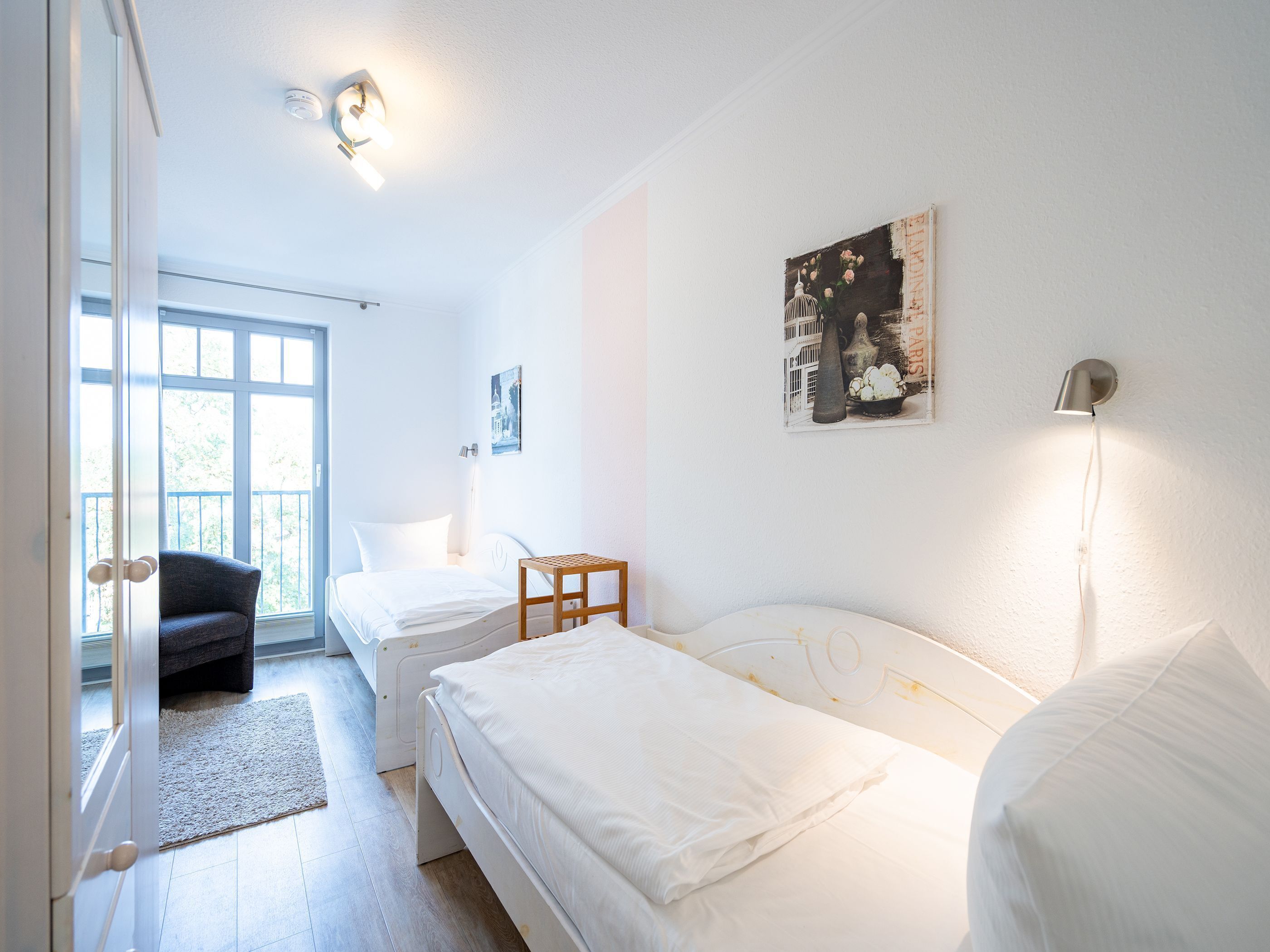 A bedroom with two beds, a chair, a small table, and a painting on the wall.