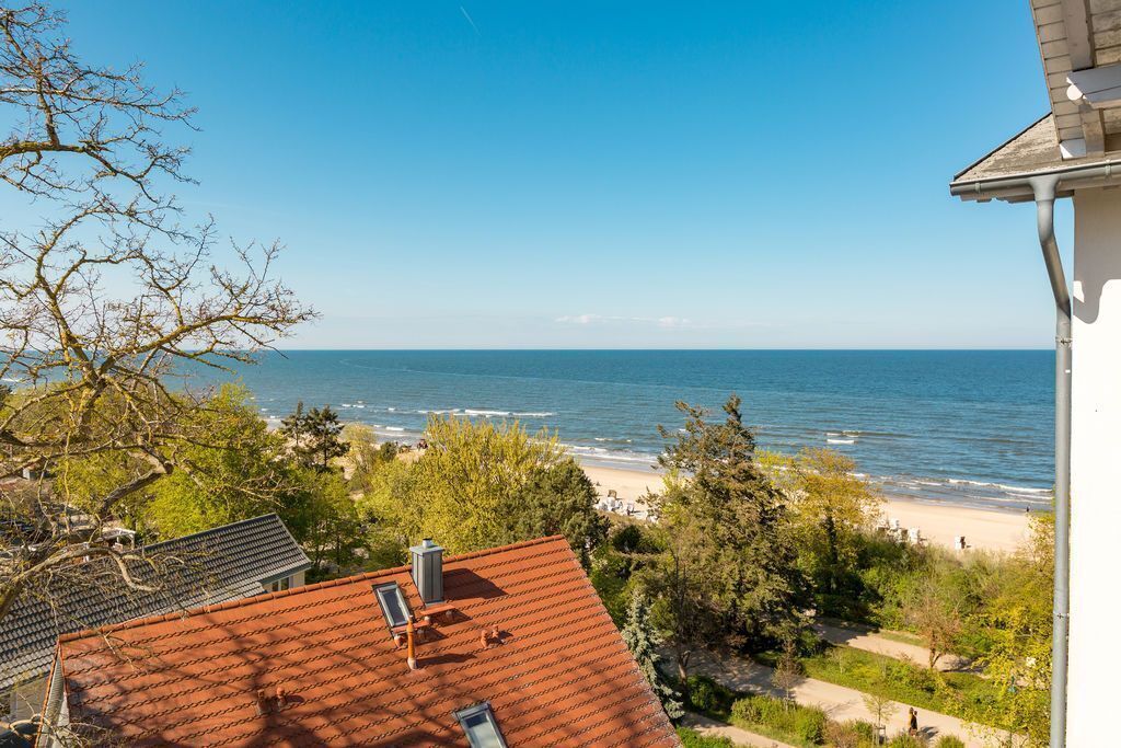 Vista costera desde un edificio con techo de tejas rojas, con vista a una playa y al mar.