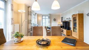 A modern living room with a wooden dining table, two wicker chairs, a television, and a cabinet. - Haus am Kliff, App. 9 (Heringsdorf)