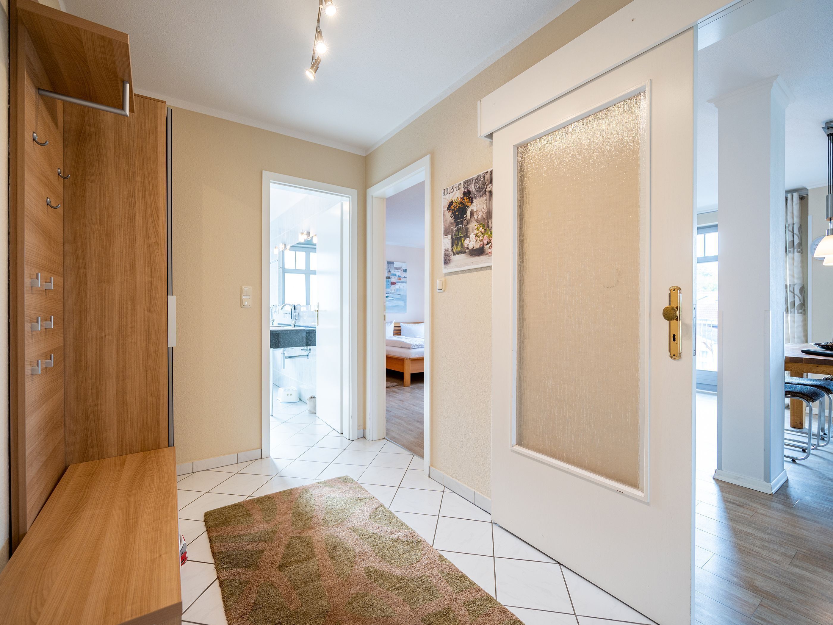 A hallway with a wooden wardrobe, a patterned rug, and a door leading to a bathroom.