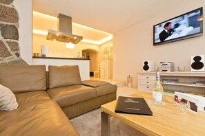A modern living room with a leather sofa, a wooden coffee table, a flat-screen TV, and a kitchen area in the background.