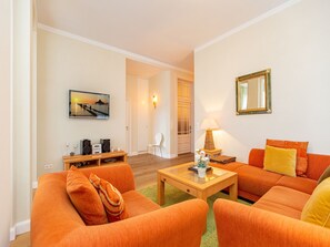 Een woonkamer met oranje banken, een salontafel, een lamp, een televisie en een schilderij aan de muur.