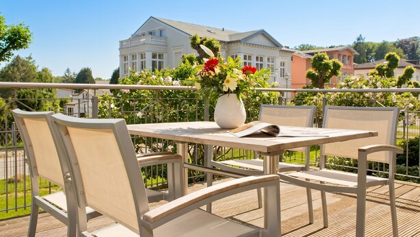 Une terrasse avec une table et des chaises, un vase rempli de fleurs et, en arrière-plan, la vue d’un grand bâtiment.