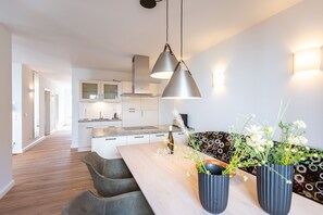 A modern kitchen with pendant lighting, a dining area with a wooden table, and a patterned sofa. - Domizil Meerzeit, App. 3 (Heringsdorf)