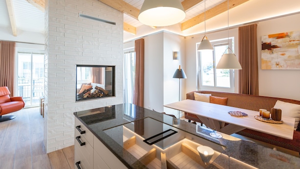 A modern kitchen with a glass island, wooden beams, and a dining area with a bench and pendant lights. - Domizil Meerzeit, App. 4 (Heringsdorf)