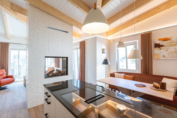 A modern kitchen with a glass island, wooden beams, and a dining area with a bench and pendant lights.