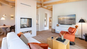 A modern living room with a fireplace, a sofa, a dining area, and a large painting on the wall. - Domizil Meerzeit, App. 4 (Heringsdorf)