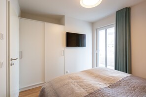 Une chambre à coucher avec un lit, une armoire, une télévision et une fenêtre avec des rideaux.