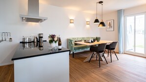 Cocina moderna con una isla central, zona de comedor con banco y un amplio ventanal que proporciona luz natural.