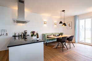A modern kitchen with a central island, a dining area with a bench, and a large window providing natural light.