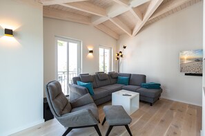 Un salon moderne avec un canapé d’angle, deux fauteuils, une table basse et un tableau accroché au mur.