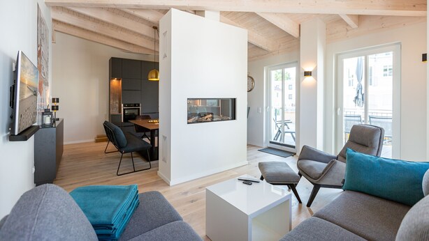 Ein modernes Wohnzimmer mit Kamin, grauen Sofas und einem Essbereich.