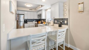Une cuisine moderne avec des meubles blancs, un îlot central et un bar pour prendre le petit-déjeuner.