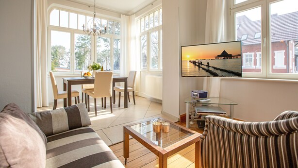 A spacious living room with a sofa, a coffee table, and a TV displaying a sunset view. - House on the Hill, The Classic 03 (Heringsdorf)