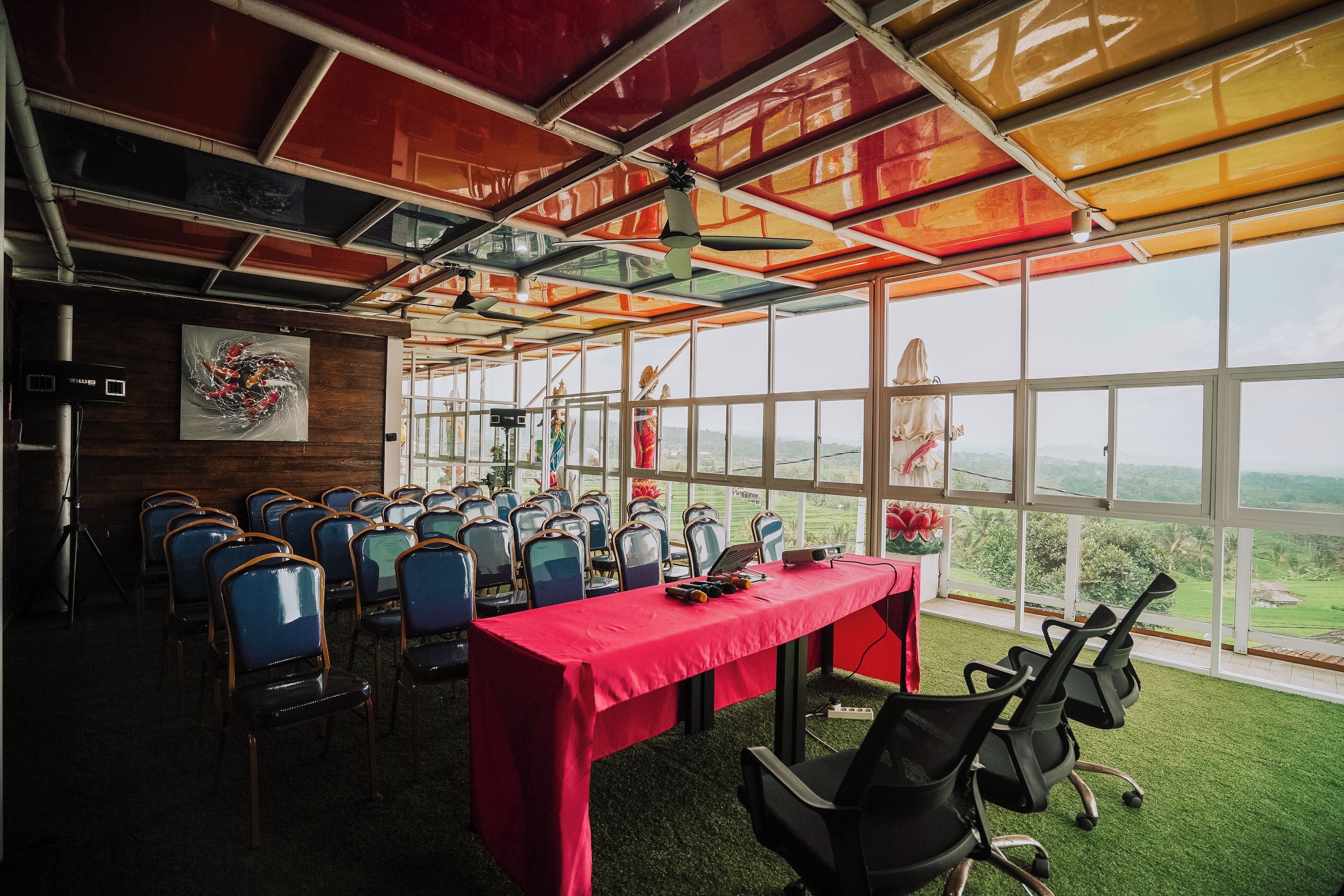 A conference room with a red table, multiple chairs, and large windows offering a view of the outdoors.