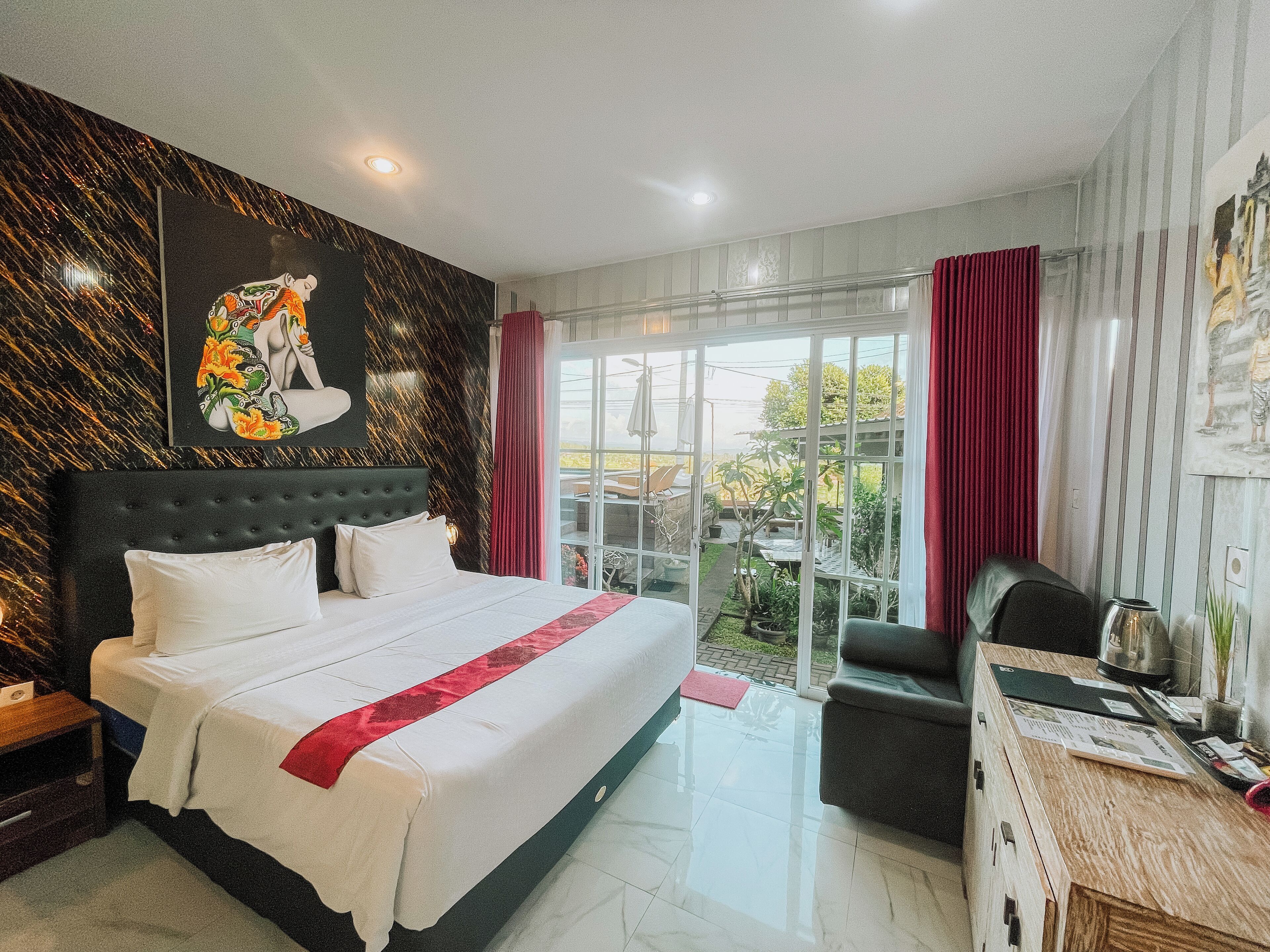 A modern hotel room with a large bed, a desk, and a view of the garden through the sliding glass door.