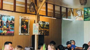 A restaurant interior with wooden beams, hanging lights, and artwork on the walls.