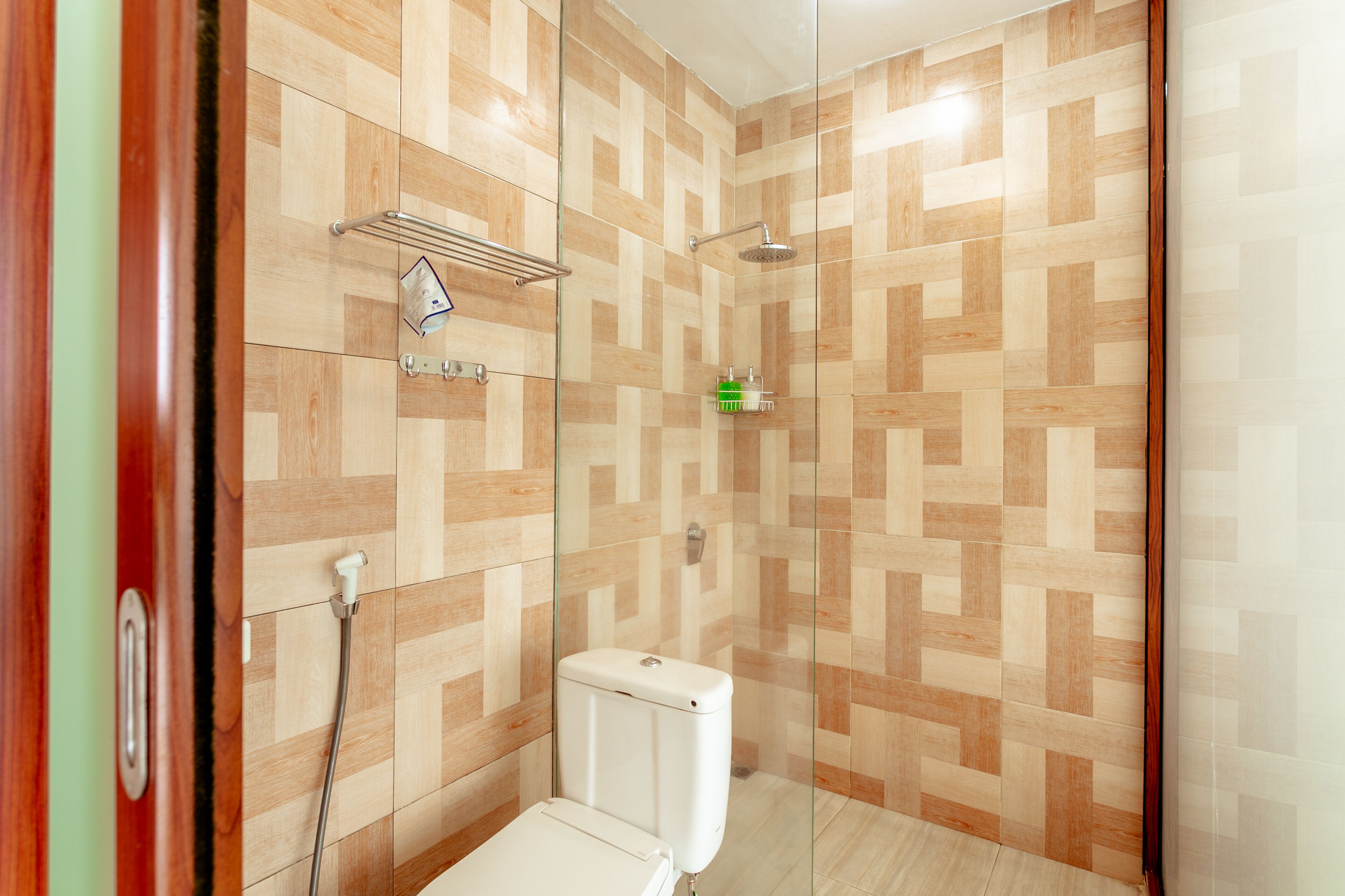 Un área de ducha con puerta de vidrio, paredes de azulejos y un inodoro.