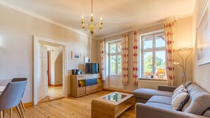 Ein Wohnzimmer mit einer Couch, einem Couchtisch, einem Fernseher auf einer Holzkommode und einer Chandelieber.