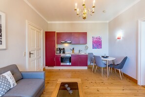 Un espacio habitable compacto con kitchenette, una zona de comedor con sillas, un sofá y una mesa de centro.