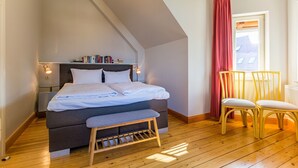 Ein Schlafzimmer mit Bett, Nachttischen, einem Bücherregal, einem Fenster mit Vorhängen und Holzboden.