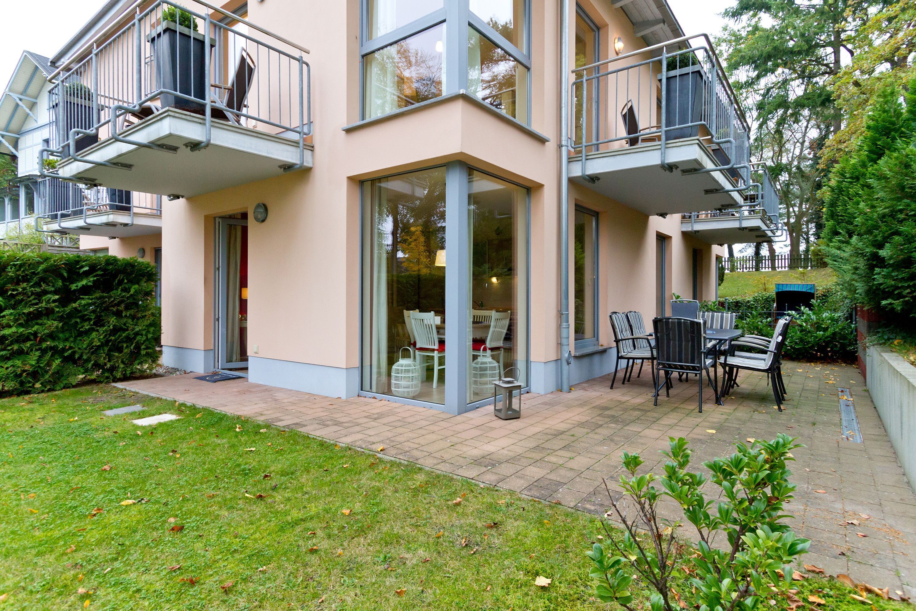 A multi-story residential building with balconies, a patio area with outdoor furniture, and a well-maintained garden.