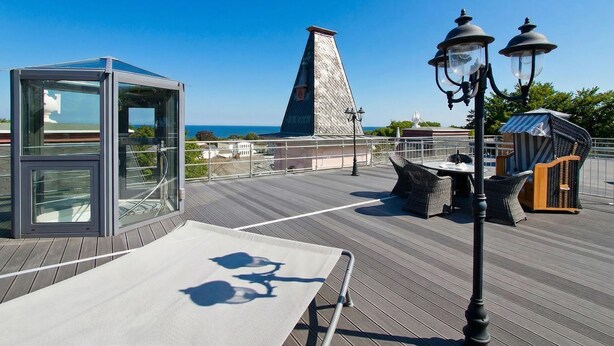 Una terraza en la azotea con cerramiento de vidrio, muebles de mimbre y vistas al mar.
