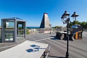 Terraço no telhado com estrutura de vidro, móveis de vime e vista para o mar.