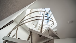 Una escalera en espiral con tragaluz, paredes blancas e iluminación en el techo.