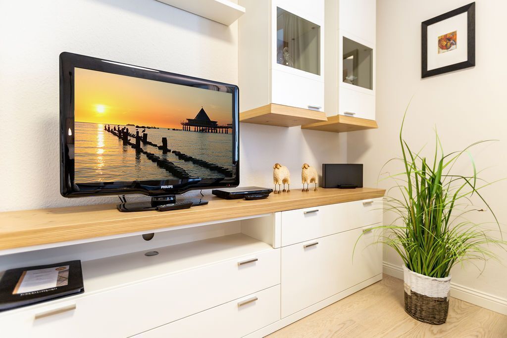 A modern living room with a flat-screen TV displaying a sunset scene, a wooden console table, white cabinetry, a small plant, and a framed picture on the wall.