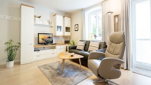 A modern living room with a sofa, a chair, a coffee table, a TV, and a bookshelf. - Villa Medici Heringsdorf, App. 02 (Heringsdorf)