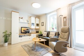 Un salon moderne comprenant un canapé, un fauteuil, une table basse, un téléviseur et une bibliothèque.