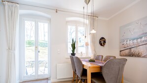 A dining area with a wooden table and chairs, a potted plant, a painting, and a view of the outdoors.