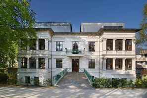 Un immeuble à étages doté d’une façade symétrique, de grandes fenêtres et d’une entrée centrale avec un escalier.