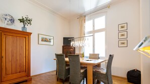 Ruokailutila, jossa on puinen pöytä, punottuista materiaaleista valmistetut tuolit, kattokruunu ja puinen kaappi.