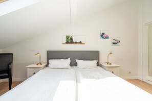 A bedroom with two beds, a desk, and a chair. There are wall-mounted lamps and artwork.
