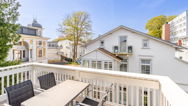 A balcony with a table and chairs, overlooking a residential area with various buildings and a tree. - Villa Hartmann-Drewitz, App. 08 (Heringsdorf)