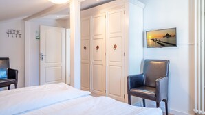 A hotel room with a large bed, a wardrobe, a chair, and a wall-mounted TV displaying a sunset scene. - Villa Hartmann-Drewitz, App. 08 (Heringsdorf)