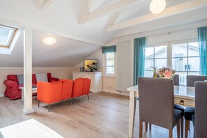 A spacious living area with a high ceiling, a dining table with chairs, a red sofa, and a view of the outside through large windows.