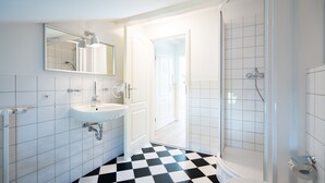 A bathroom with a white sink, mirror, and shower. The floor has a black and white checkered pattern. - Villa Hartmann-Drewitz, App. 08 (Heringsdorf)