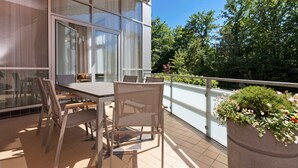 Ein Balkon mit Tisch und Stühlen, einem Blumentopf und Blick auf Bäume und ein Gebäude.