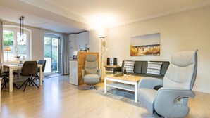 A modern living room with a sofa, armchairs, a coffee table, and a dining area with a table and chairs. - Villa Medici Heringsdorf, apt. 01 (Heringsdorf)