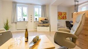 A modern living room with a dining table, chairs, a sofa, a TV, and a window with curtains. - Villa Medici Heringsdorf, apt. 01 (Heringsdorf)