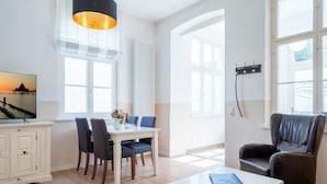A spacious living room with a dining area, large windows, a white radiator, and a black pendant light. - Villa Hartmann-Drewitz, App. 03 (Heringsdorf)