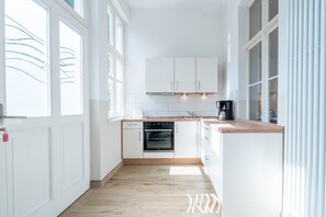Une cuisine moderne avec des meubles blancs, un four encastré et un plan de travail en bois.