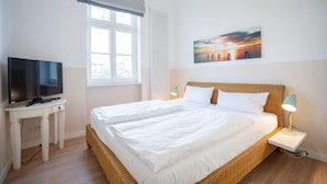 A bedroom with a large bed, a television on a white table, and a painting on the wall. - Villa Hartmann-Drewitz, App. 03 (Heringsdorf)