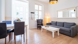 A modern living room with a grey sofa, a white coffee table, and a dining area with blue chairs. - Villa Hartmann-Drewitz, App. 03 (Heringsdorf)
